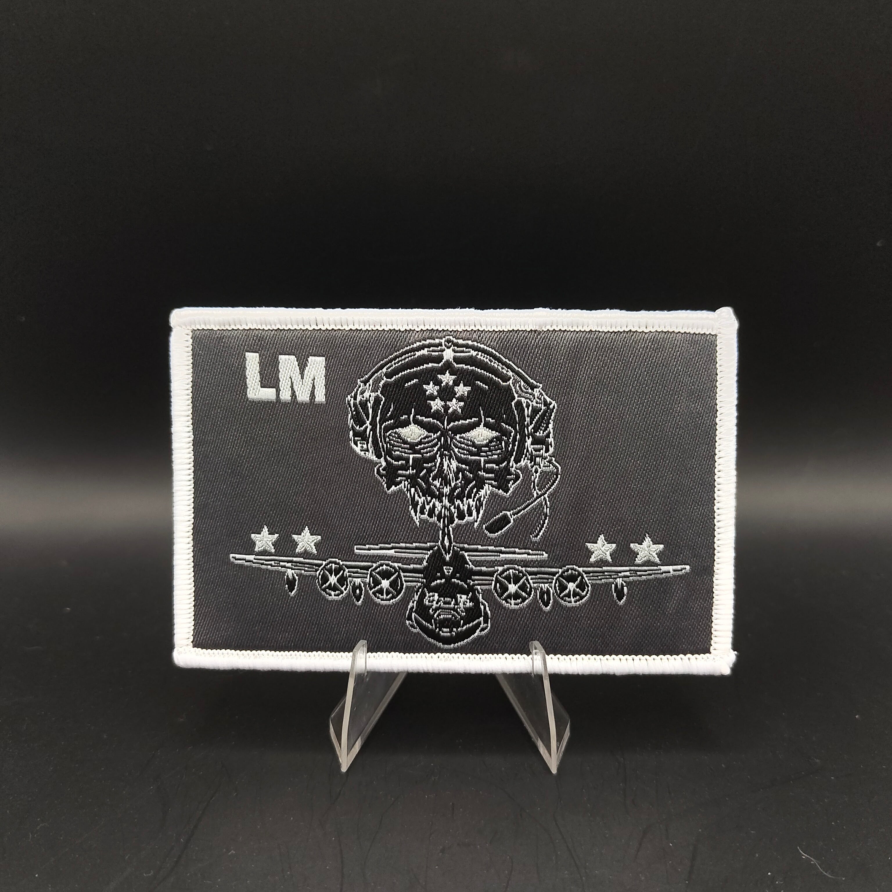 Black and white patch with skull design and 'LM' initials on a stand against a black background loadmaster aircrew kc-130j c-130 crew patch